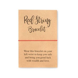 May include: Red string bracelet on a brown card with the text "Red String Bracelet" and "Wear this bracelet on your left wrist to keep you safe and bring you good luck with wealth and love."