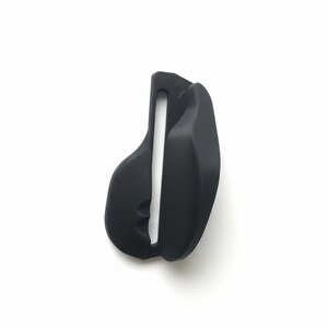 Op de afbeelding: Een zwart, zadelvormig object met een centrale verticale opening. Het object heeft aan één kant een textuuroppervlak en aan de andere kant een gladde afwerking. Het ontwerp suggereert een focus op comfort en ondersteuning.