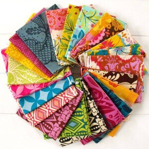 May include: A circular arrangement of colorful fabric squares. The fabrics feature various floral and geometric patterns in shades of pink, blue, yellow, and green. The arrangement is on a white surface.