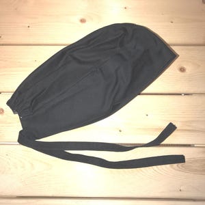 May include: A black surgical scrub cap with a gathered elastic band and long ties. The cap is made of a soft, breathable fabric.