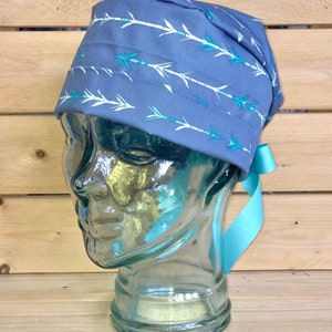May include: A blue scrub hat with a white and teal arrow pattern. The hat has a light blue ribbon tie.