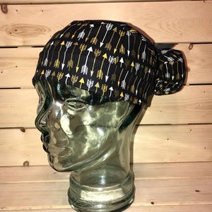 May include: Black scrub hat with a pattern of gold and white arrows. The hat is tied at the back with a black ribbon.