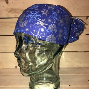 May include: A blue scrub hat with a silver snowflake pattern. The hat is on a glass head form.