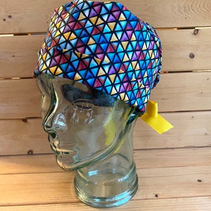May include: A blue, yellow, red, and purple patterned surgical scrub hat with a yellow tie. The hat is made of a soft, breathable fabric and is designed to be comfortable to wear for long periods of time.