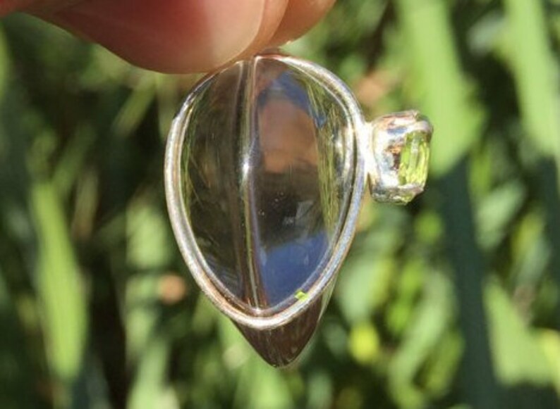 Pu&ograve; includere: Un ciondolo d'argento con un cristallo di quarzo trasparente e una piccola pietra preziosa verde. Il ciondolo ha la forma di una lacrima e ha un'anellina in argento.