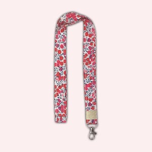 May include: A white lanyard with a red and pink floral pattern and a gold accent. The lanyard has a silver swivel clip.