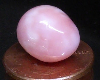 May include: A large, pink, oval-shaped pearl resting on a copper penny.