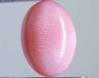 May include: A polished, oval-shaped gemstone in a soft pink hue, held by a pair of silver tweezers. The gem has a smooth, glossy surface with subtle internal patterns. The gemstone is approximately 1 inch in length.
