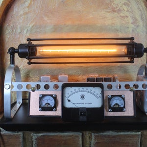 May include: A steampunk-style table lamp with a caged light bulb, three analog gauges, and a black base. The gauges are labeled "MILLIAMPERE SECONDS".