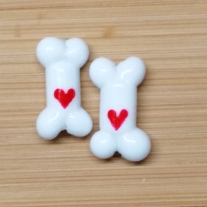 May include: Two white ceramic dog bone-shaped charms with red heart accents.