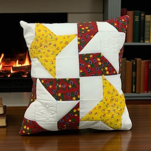 May include: Square throw pillow with a patchwork design. The pillow features white, yellow floral, and red floral fabric. The design includes star and square patterns. The pillow is placed on a wooden surface.