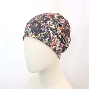 Può includere: Un berretto nero con una stampa floreale con fiori rosa, gialli e blu. Il berretto è realizzato in un tessuto morbido ed elastico.