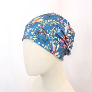 Può includere: Un berretto blu con una stampa floreale con fiori rosa, gialli e bianchi. Il berretto è realizzato in un tessuto morbido ed elastico.