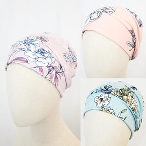 Può includere: Tre fasce per capelli con stampa floreale in rosa, azzurro e rosa. Ogni fascia presenta un motivo floreale diverso con fiori bianchi e blu. Le fasce per capelli sono esposte su teste di manichino su sfondo bianco.