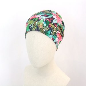 Può includere: Un berretto con stampa floreale con fiori rosa, foglie verdi e dettagli bianchi su uno sfondo blu navy scuro. Il cappello è esposto su una testa di manichino, mostrando la sua forma e il suo design.