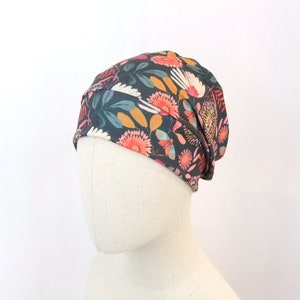 Può includere: Un berretto grigio scuro con una stampa floreale con fiori rosa, arancioni e gialli su uno sfondo verde scuro.