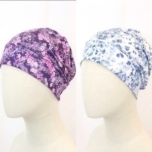 Può includere: Due berretti a maglia con stampa floreale, uno in viola e rosa e l'altro in blu e bianco.