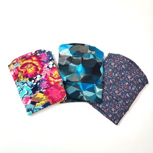 Può includere: Tre fasce per capelli in tessuto con diversi motivi. Una ha un vivace motivo floreale con fiori rosa, gialli e blu su sfondo blu navy. Un'altra presenta un motivo geometrico astratto blu e grigio. La terza ha una piccola stampa floreale su sfondo blu navy.