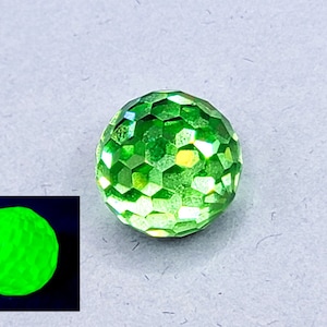 Puede incluir: Una gema verde facetada que brilla de un verde brillante bajo una luz negra.