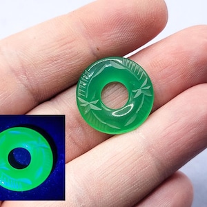 May include: A green jade ring with a carved design. The ring glows a bright green under a black light.