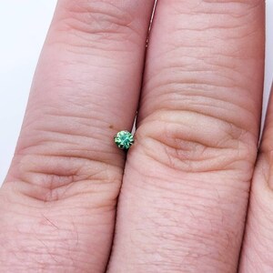 May include: A small, round, green gemstone with a faceted surface.