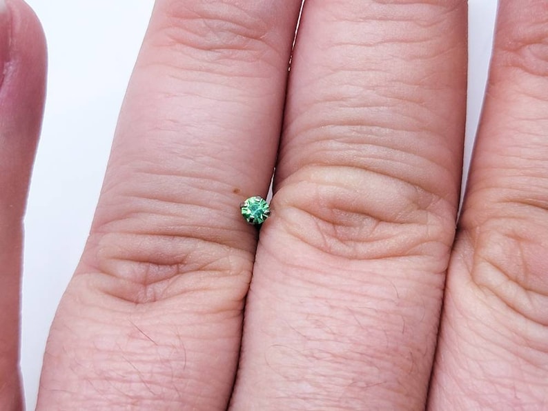 May include: A small, round, green gemstone with a faceted surface.