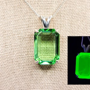 May include: A silver chain necklace with a green emerald-cut pendant. The pendant glows green under a black light.