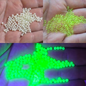 May include: A collection of small, spherical beads shown in three states: opaque white beads, translucent neon yellow beads, and the same beads glowing with a bright, intense green light under ultraviolet illumination.