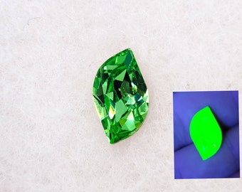 Può includere: Una gemma verde con taglio a faccette, a forma di foglia. La gemma brilla di un verde brillante sotto la luce UV.