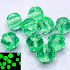 May include: Nine green glass beads with a swirl pattern. The beads glow in the dark.