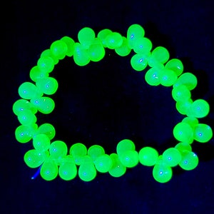 K&ouml;nnte beinhalten: Eine Kette aus leuchtend gr&uuml;nen Glasperlen, die auf einem schwarzen Hintergrund zu einem Kreis angeordnet sind.
