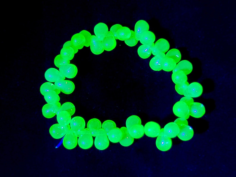 K&ouml;nnte beinhalten: Eine Kette aus leuchtend gr&uuml;nen Glasperlen, die auf einem schwarzen Hintergrund zu einem Kreis angeordnet sind.