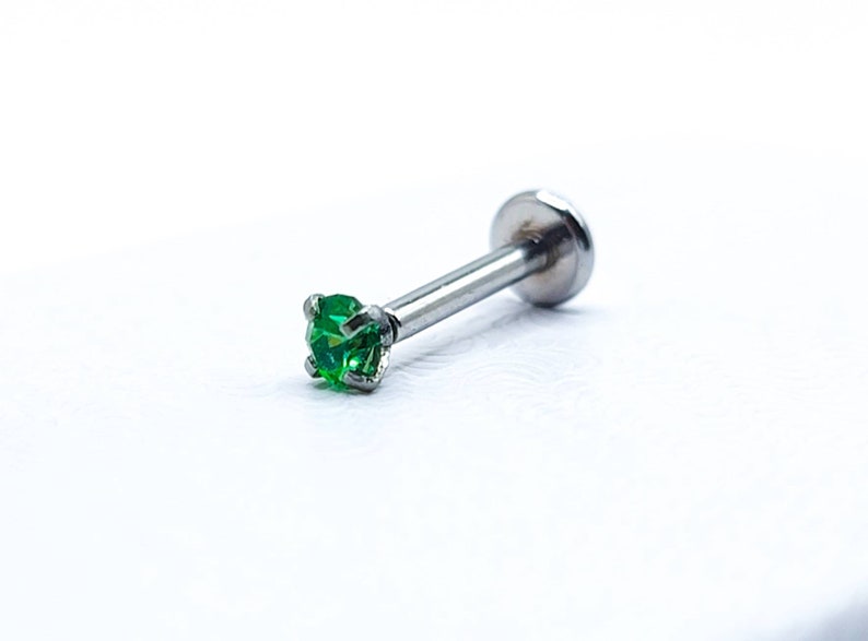 May include: A silver body piercing with a small green gem. The piercing is made of surgical steel and is suitable for a variety of body piercings.
