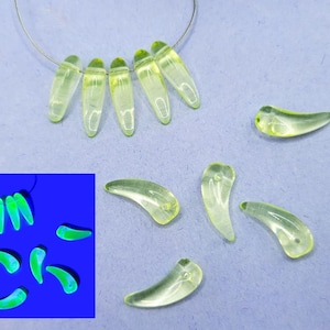 May include: A collection of 10 clear glass beads in a light green color. The beads are shaped like a crescent moon and are strung on a wire. The beads glow a bright green under a black light.