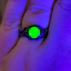 May include: A black ring with a large, bright green gemstone set in a skull-shaped design.