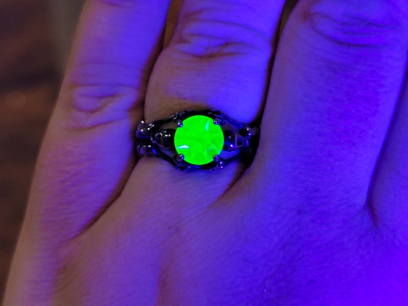 May include: A black ring with a large, bright green gemstone set in a skull-shaped design.