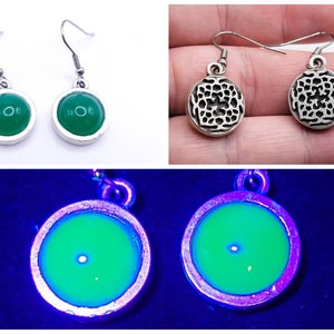 May include: Three pairs of earrings are shown. Two pairs feature a silver-coloured metal frame with a green, round stone. The third pair has a silver-coloured metal frame with a green, round stone that glows under a black light. The third pair has a patterned design.