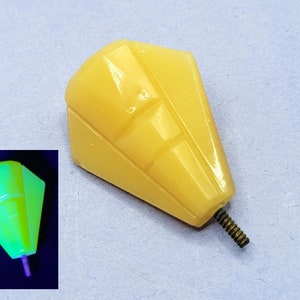 May include: A yellow glass knob with a geometric design. The knob has a screw on the bottom. The knob glows green under a black light.