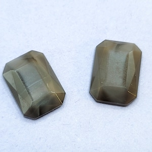 May include: Two dark gray faceted glass stones with a rectangular shape.
