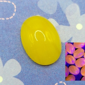 May include: A bright yellow, oval-shaped gemstone is the focal point, set against a blue floral patterned background. A smaller inset image shows multiple similar stones with a glowing effect. The stone's smooth surface reflects light.