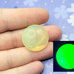 May include: A round, translucent yellow cabochon with a faint, swirling pattern inside. The cabochon glows bright green under a blacklight.