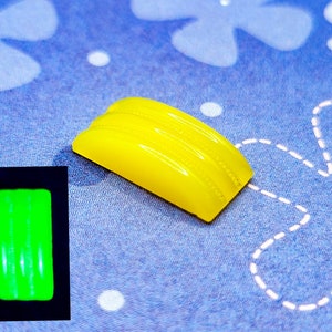 May include: A yellow plastic button with a textured surface. The button glows green in the dark.