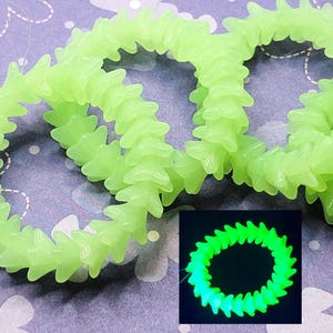 May include: A close-up of a string of glow-in-the-dark beads. The beads are shaped like stars and are strung together in a circle. The beads are a light green colour and are glowing in the dark. The beads are shown in a close-up view, with the background blurred.