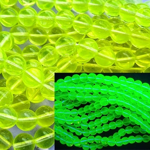 May include: A strand of bright yellow glass beads that glow green under a black light. The beads are round and smooth.