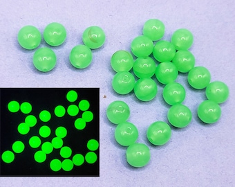 May include: A group of 20 small, round, green beads. The beads are translucent and have a slight glow in the dark effect. The beads are scattered on a light blue surface.