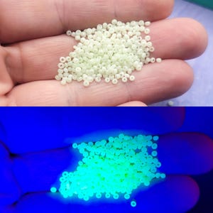 May include: A collection of small, round, off-white beads. The beads glow bright green under a black light. These beads are likely used for jewellery making or other crafts.