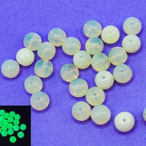 May include: A collection of round, off-white beads with a hole through the center. Some beads have a subtle, iridescent quality. A smaller image shows the beads glowing bright green.