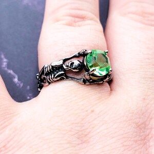 May include: A silver ring with a skeleton design holding a large green gemstone.