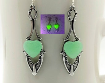 May include: A pair of silver dangle earrings with a light green heart-shaped glass charm. The charms glow in the dark.