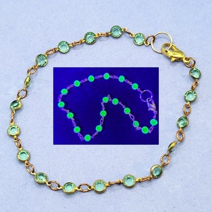 May include: A delicate gold chain bracelet with small, round, light green gemstones. The bracelet is shown under a UV light, revealing the gemstones' bright green fluorescence.